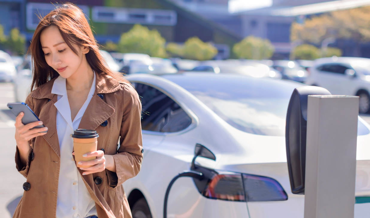 woman charging car and looking at phone