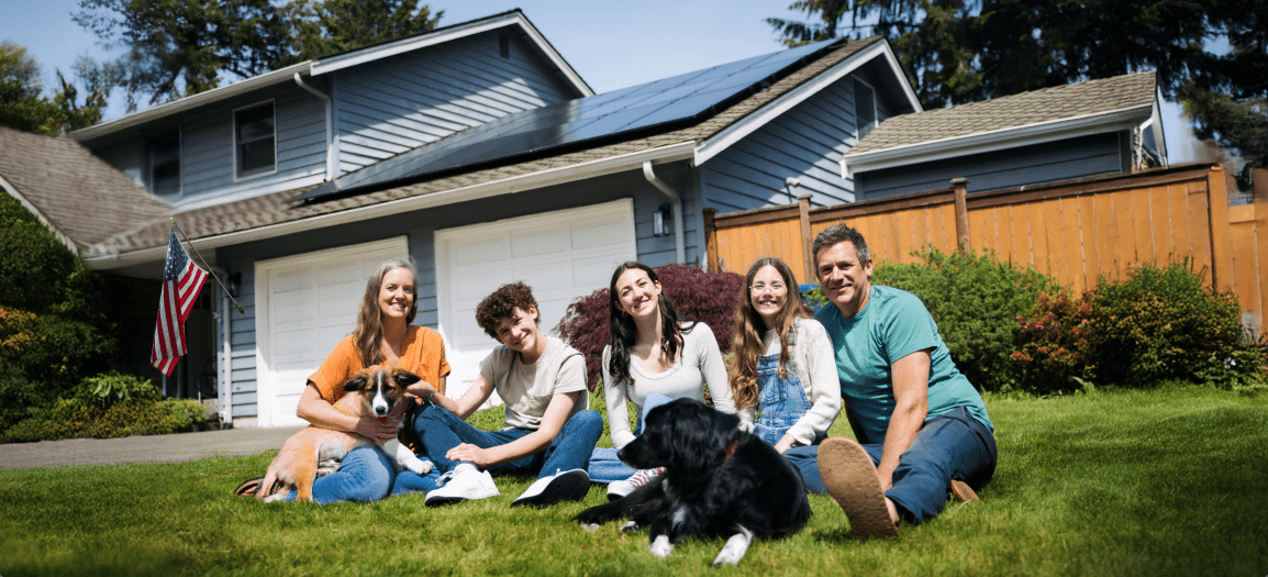 An American family sitting in front of their home with solar panels on the roof